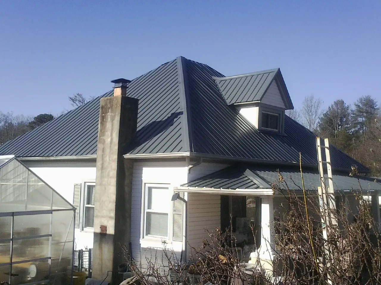 Dark blue standing seam metal roof on a white farmhouse with dormer — Slate & Tile Roof Repair by Roofing Brothers in Blue Point