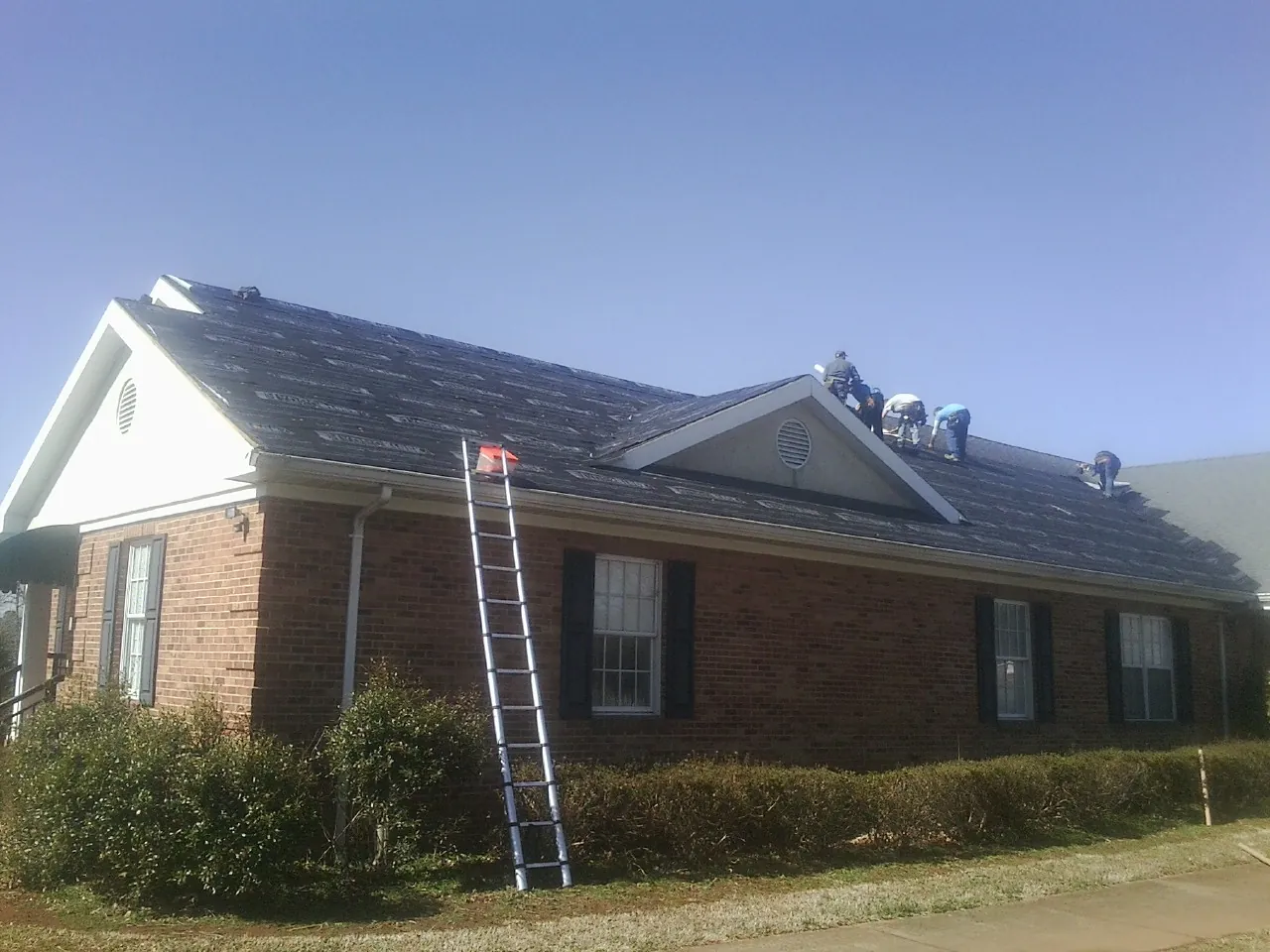 Crew tearing shingles off a brick ranch roof with a ladder set — Metal Roof Repair work by our crew in Blue Point