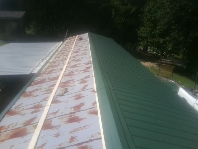 Old rusted panels beside newly installed green metal roofing — Wind Damage Roof Repair by Roofing Brothers in Blue Point