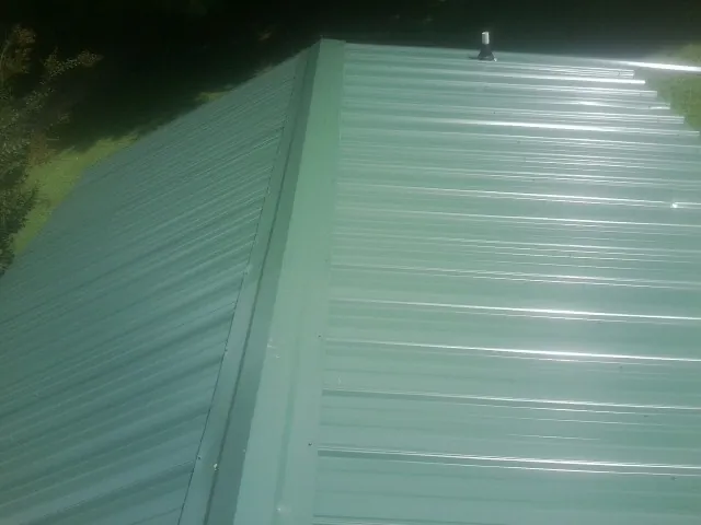 New green metal panels meeting at the ridge of a roof — Flat Roof Repair work by our crew in Blue Point