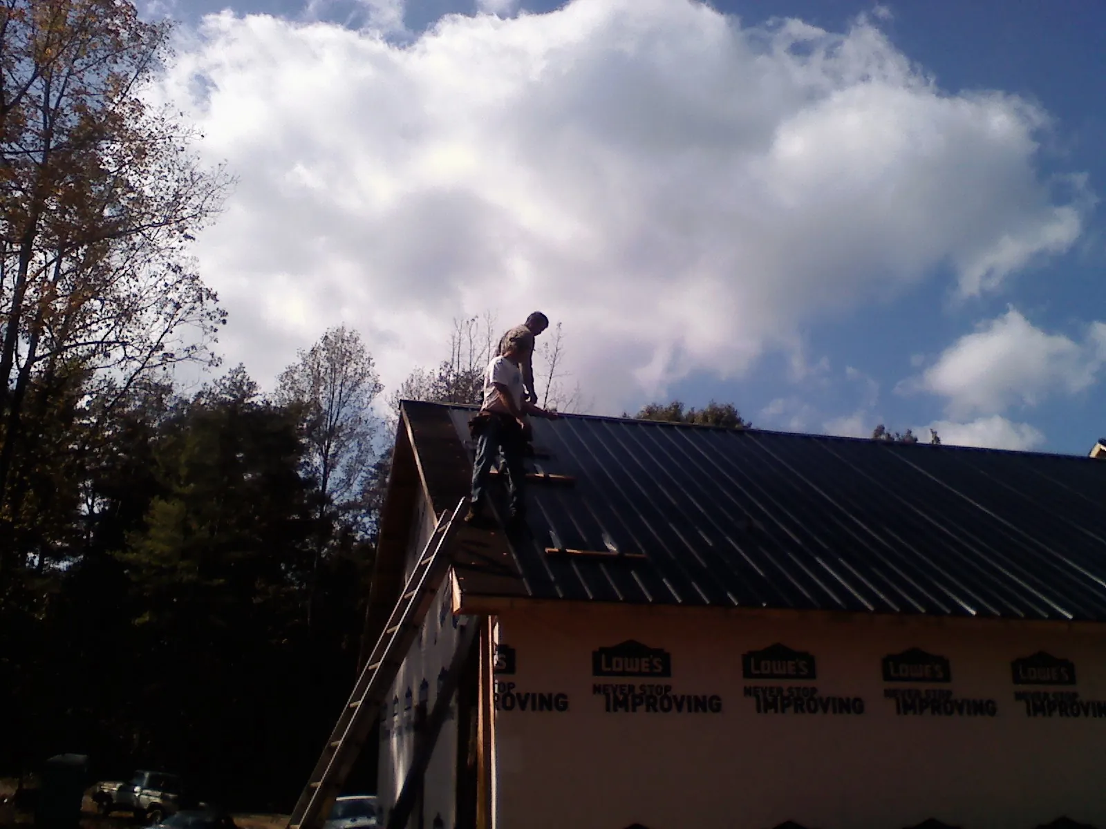 Roofer fastening dark metal panels high against a cloudy sky, from a Roof Inspection job in Blue Point
