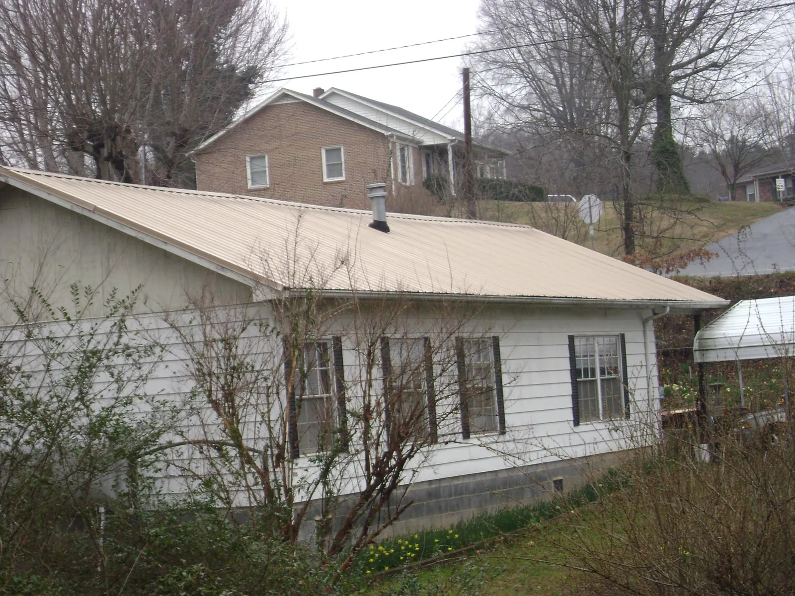 Tan metal roof on a white sided house set into a hillside — Commercial Roofing by Roofing Brothers in Blue Point