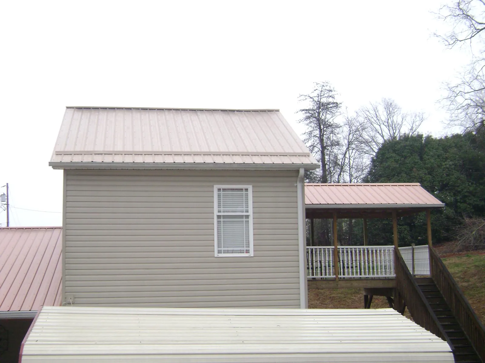 Tan metal roofs on a two story addition and attached porch, from a Roof Replacement job in Blue Point
